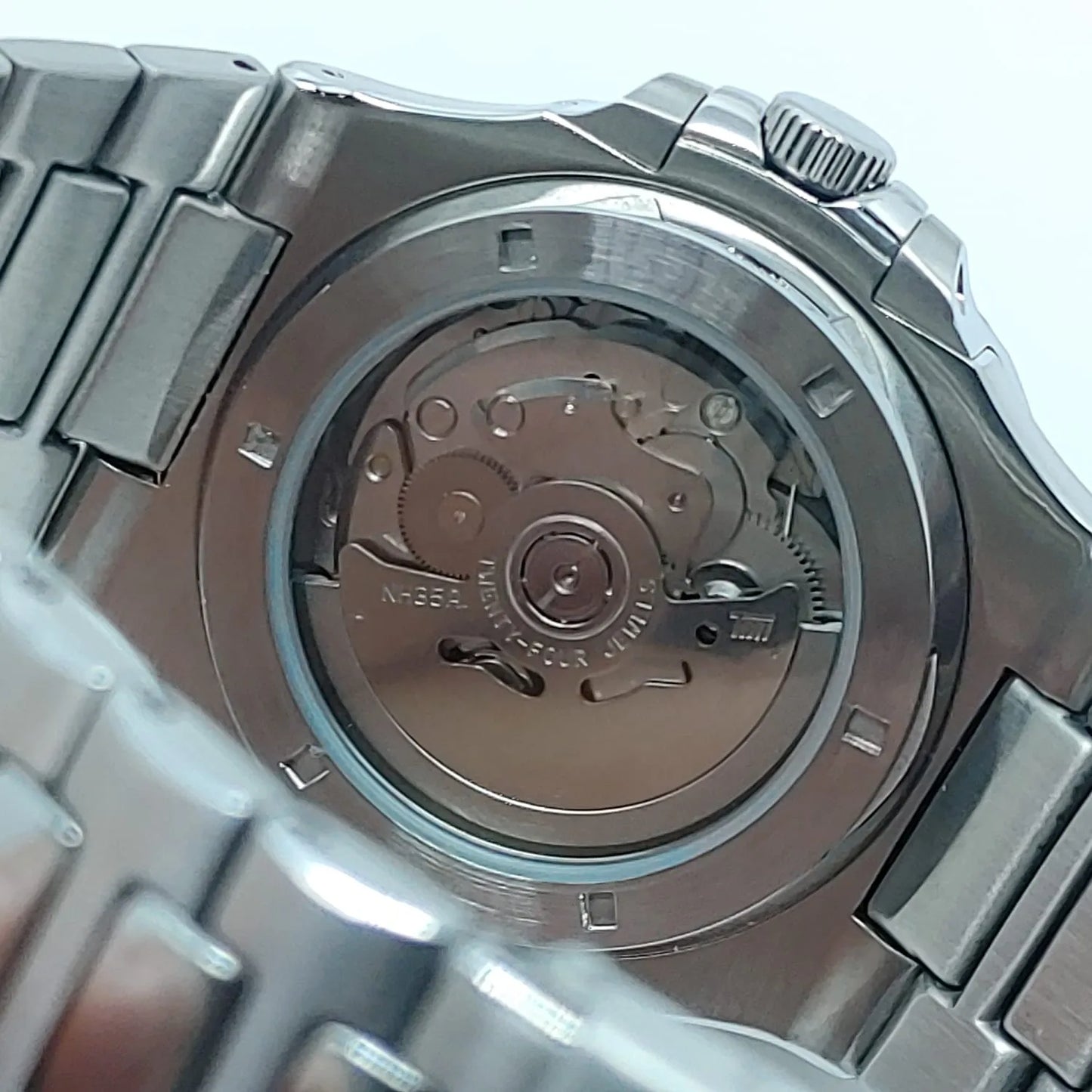 Stainless steel watch back with visible automatic movement and engraved rotor, integrated metal bracelet links.