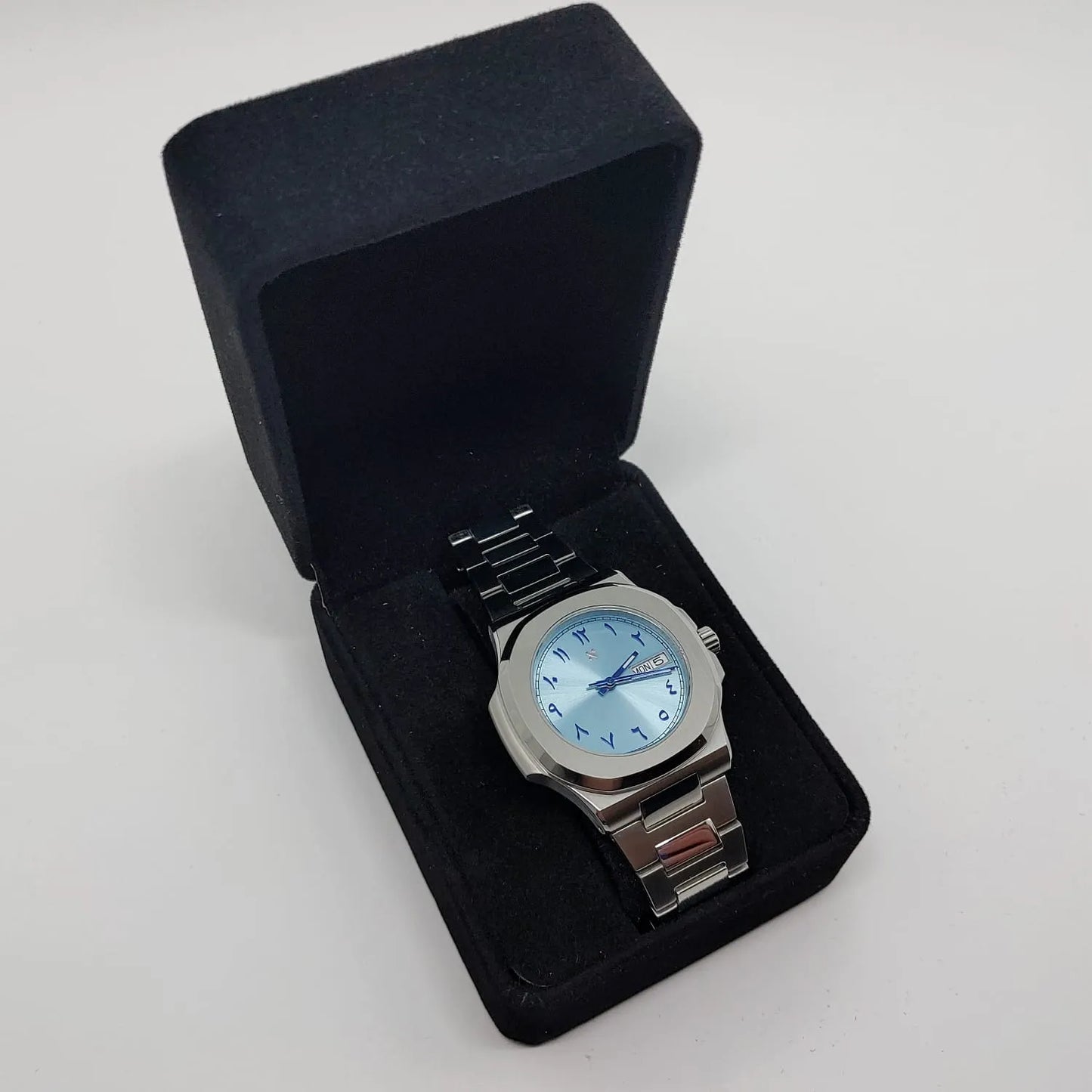 Seiko 40mm stainless steel watch with ice blue Arabic dial, day-date window, and metal bracelet in black presentation box.