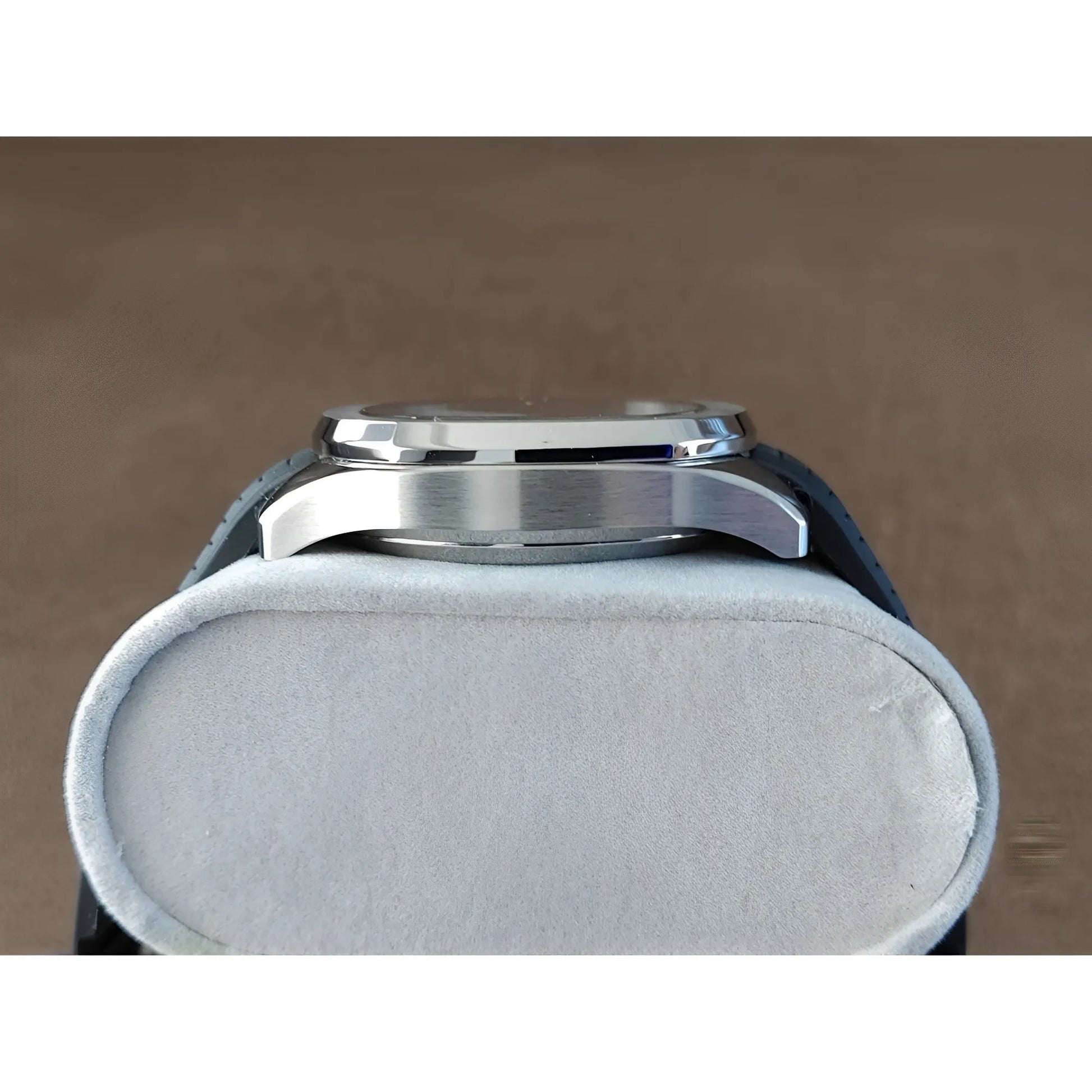 Side view of a sleek stainless steel watch case with polished finish on a white cushion.