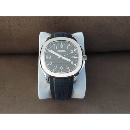 Seiko Aquanaut watch with black textured dial, silver case, white numerals, and black rubber strap on white cushion.
