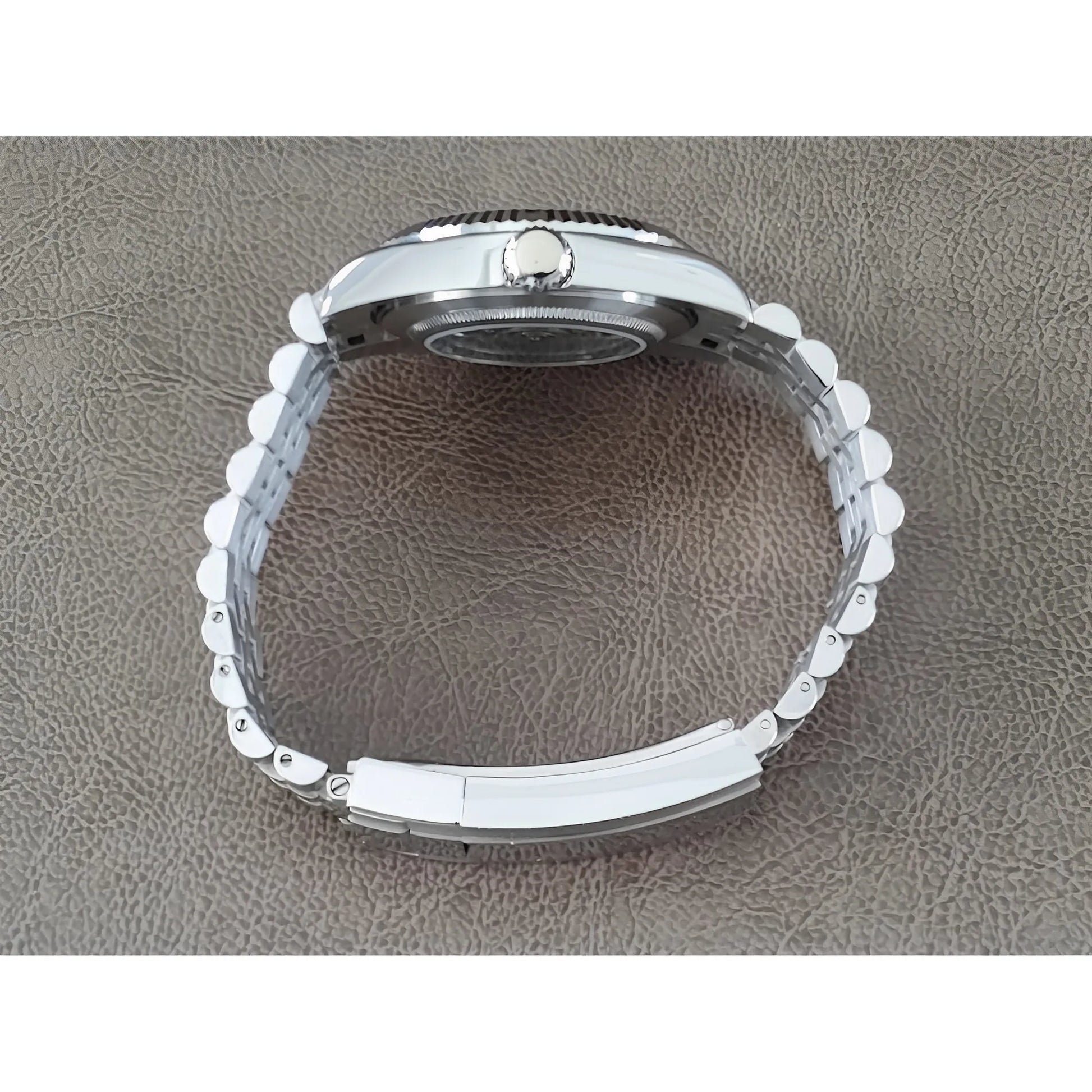 Silver stainless steel watch bracelet and case side with fluted bezel on brown textured surface.