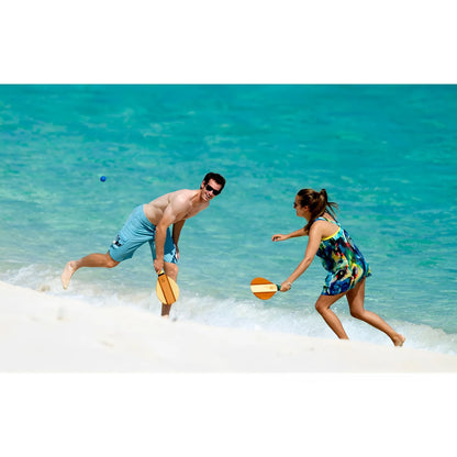 Wooden paddleball set with orange and white paddles held by two players on a sandy beach by turquoise water.
