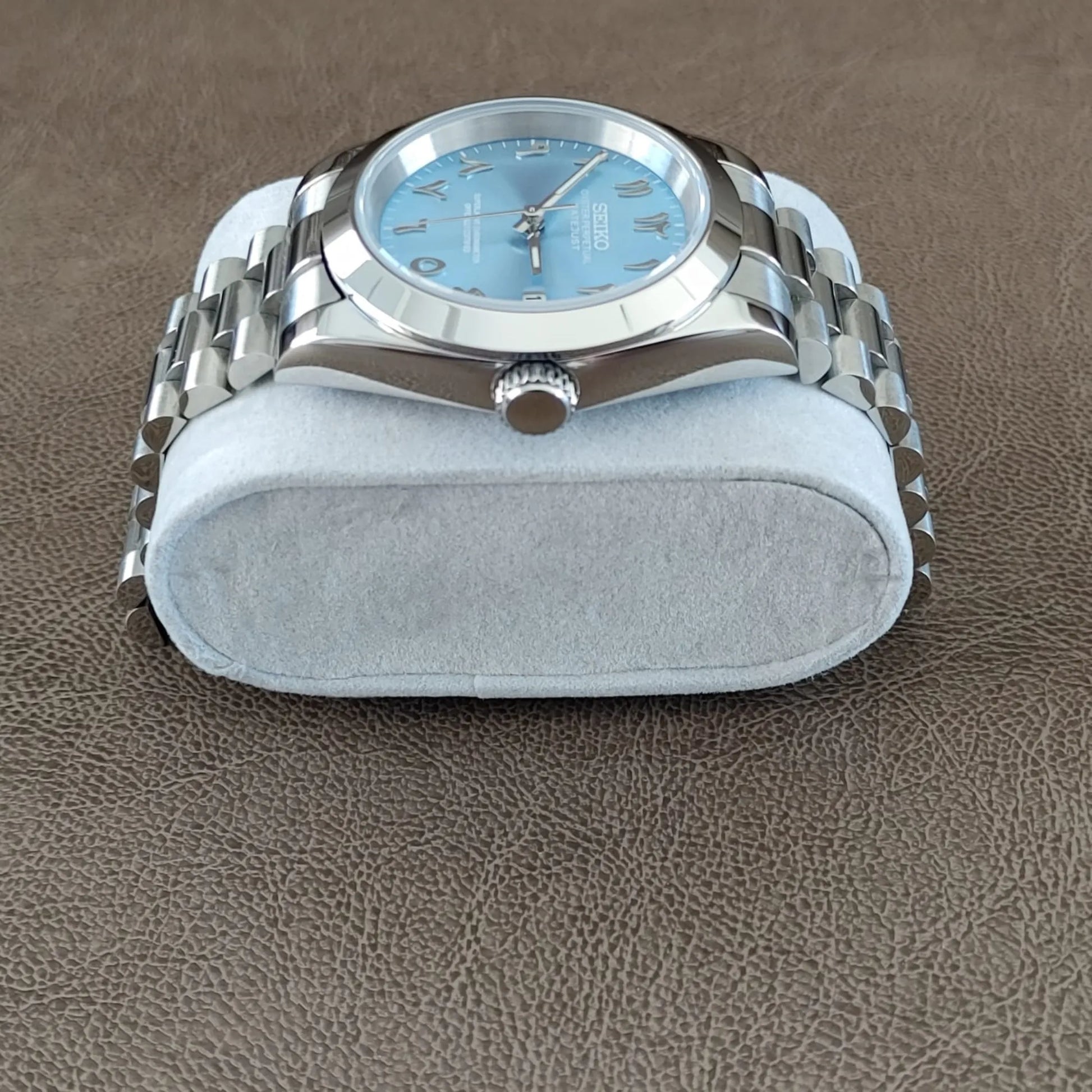 Seiko wristwatch with 39mm platinum case, fluted bezel, ice blue dial, Arabic numerals, and silver Jubilee bracelet on gray.
