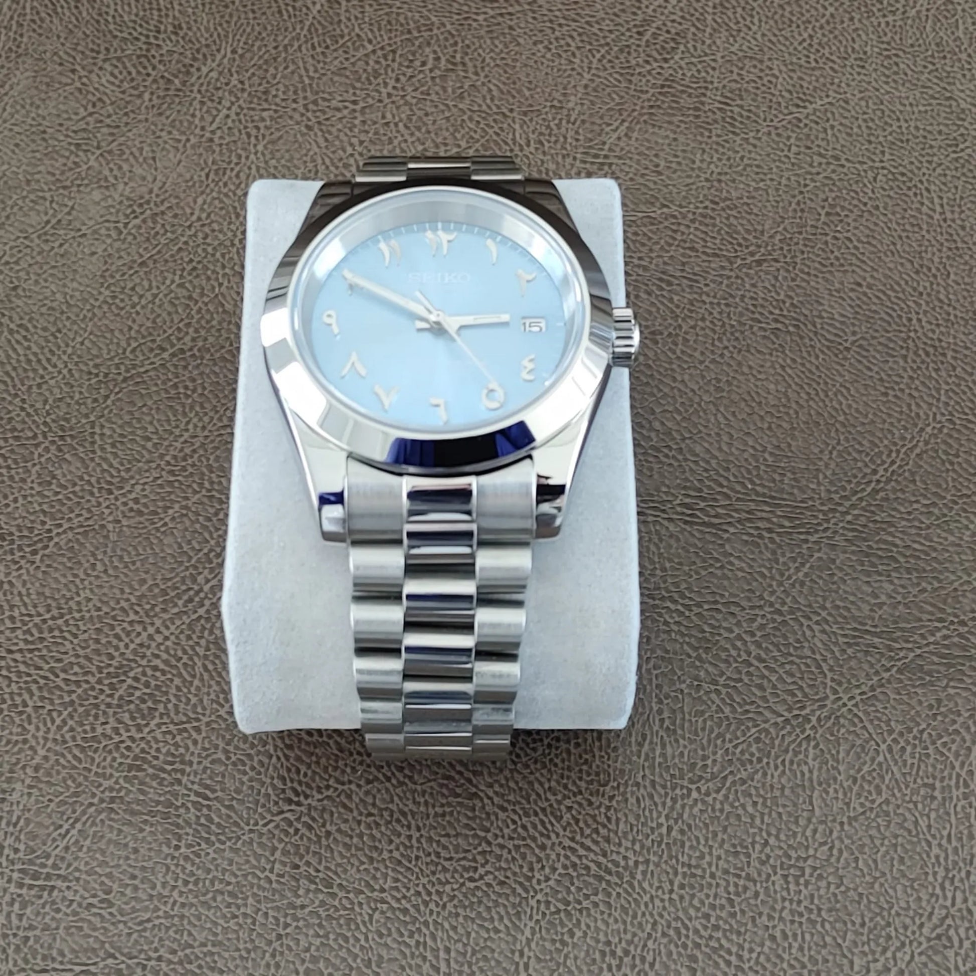 Seiko watch with 39mm platinum case, fluted bezel, ice blue dial, silver Arabic numerals, and stainless steel Jubilee.
