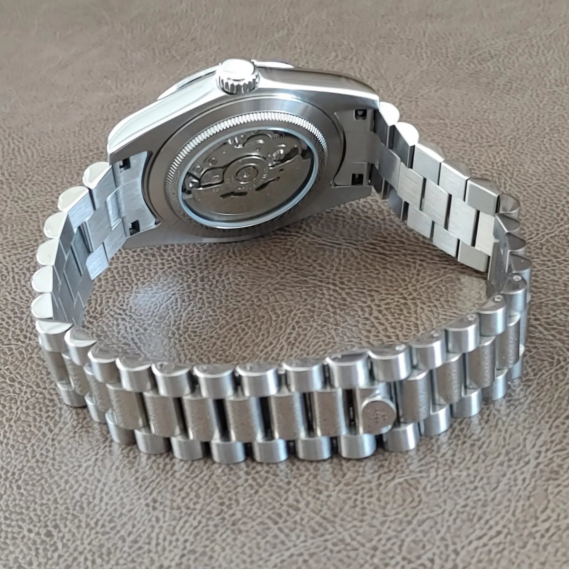 Seiko NH35 wristwatch with silver stainless steel President strap and transparent case back showing movement.