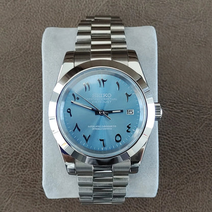 Seiko NH35 wristwatch with ice blue dial featuring Arabic numerals and date window, stainless steel President bracelet.