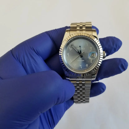 39mm silver stainless steel watch with fluted bezel, ice blue dial, white Arabic numerals, and date window at 3 o'clock.