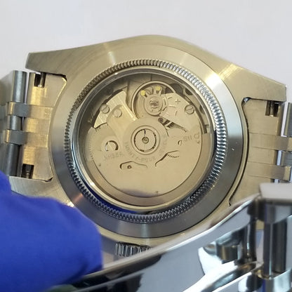 Back view of stainless steel watch with transparent case back showing mechanical movement and polished bracelet links.