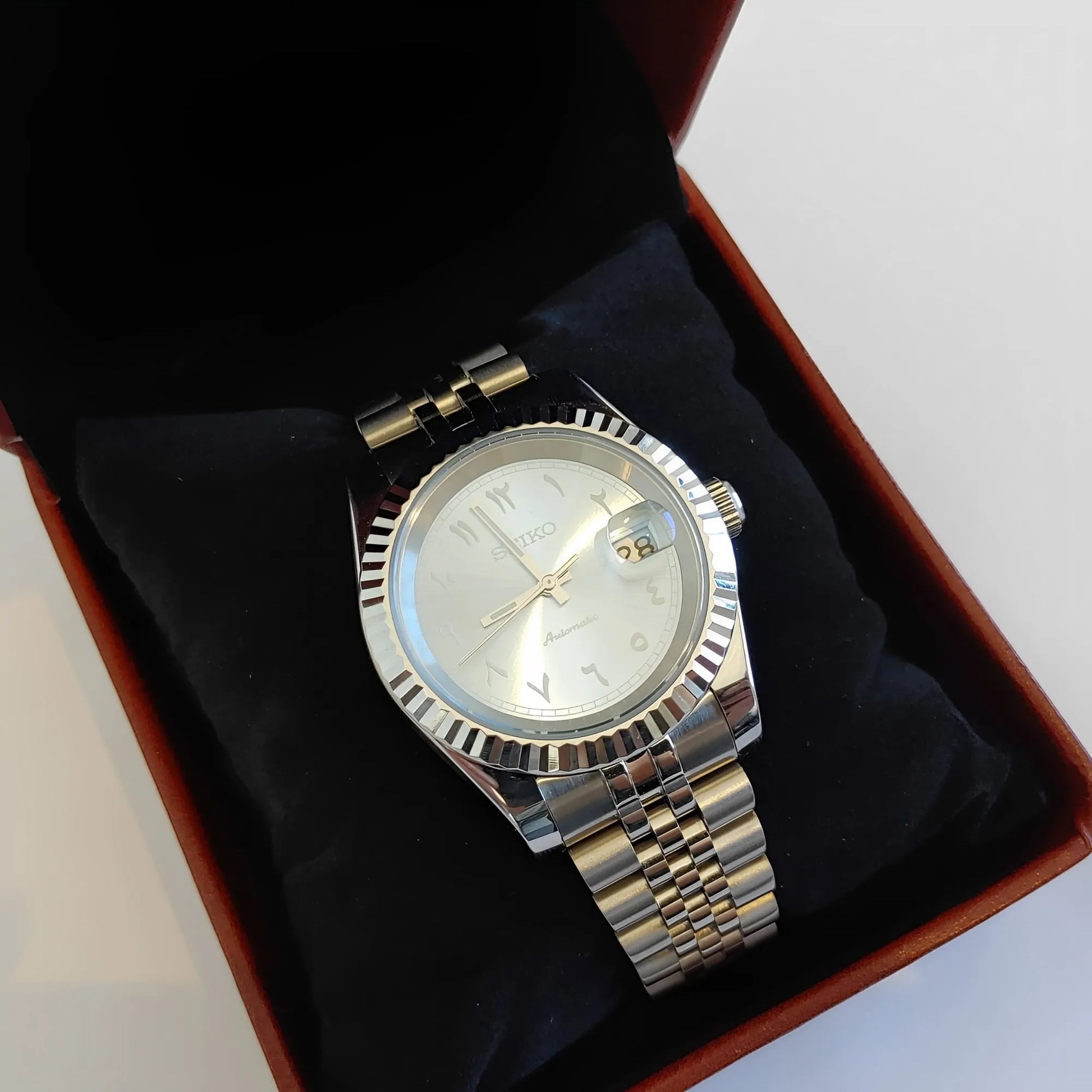 Silver stainless steel watch with fluted bezel, ice blue dial, white Arabic numerals, and two-tone metal bracelet displayed.