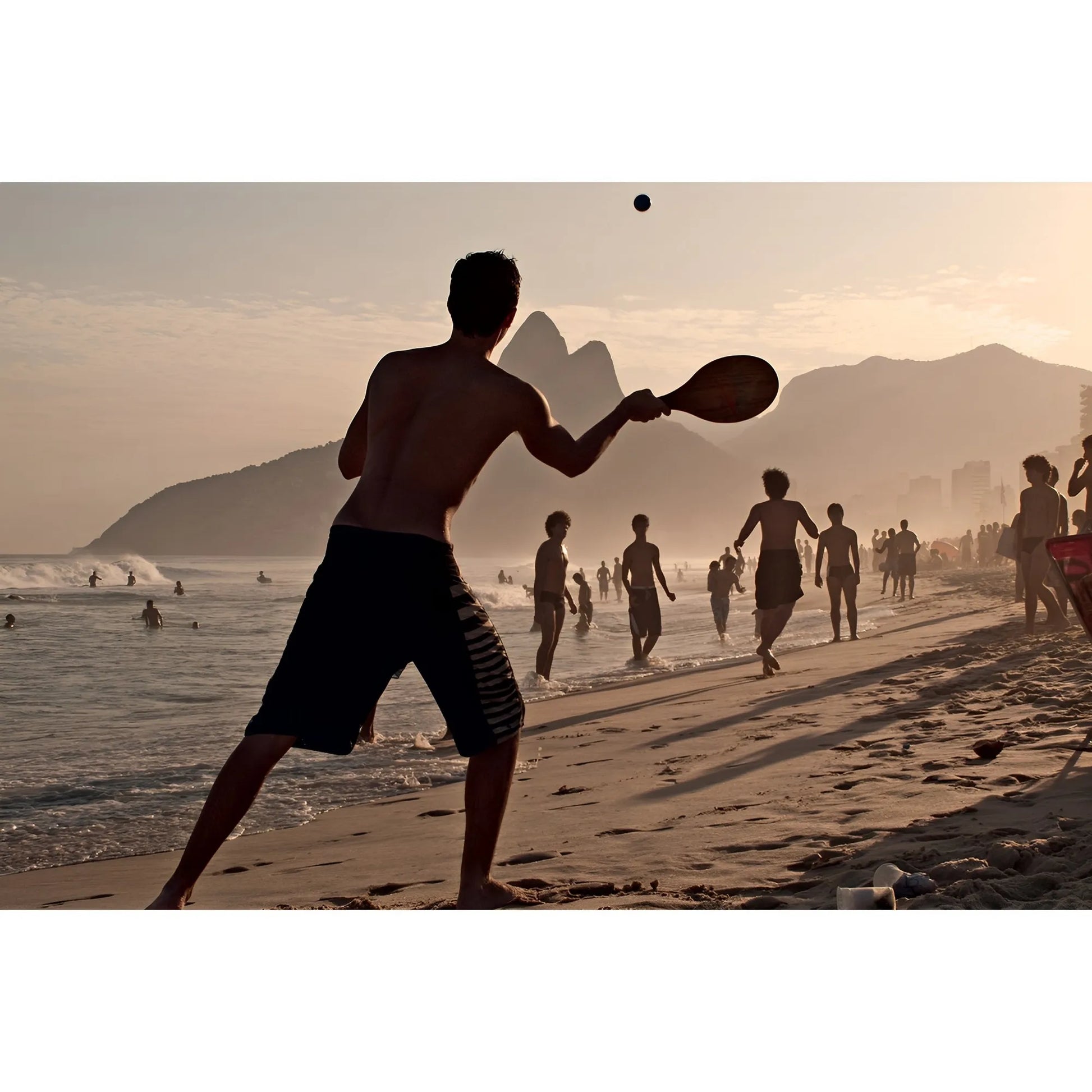 Wooden paddleball set with smooth handles and a black paddle hitting a small black ball on a sunny beach.