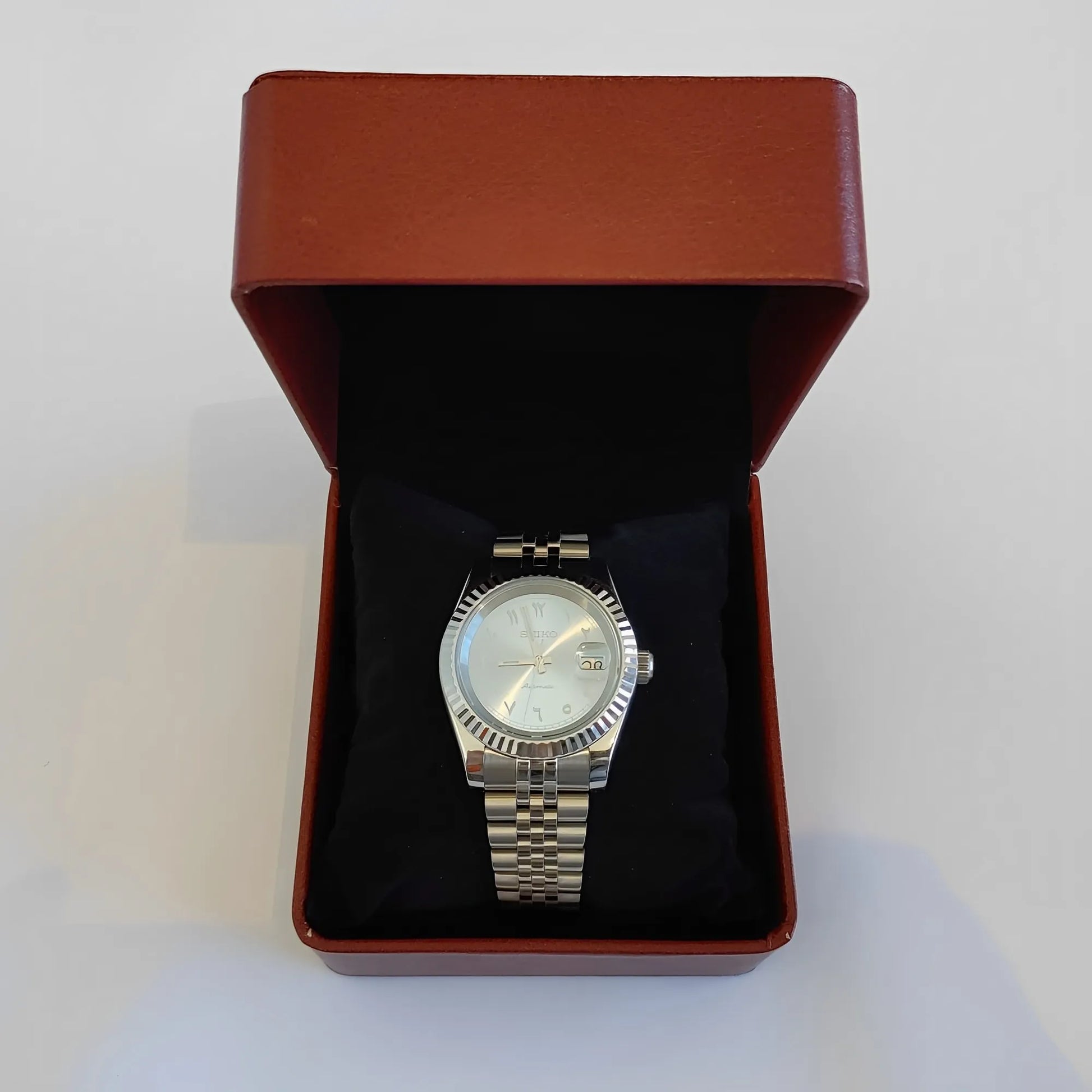 Silver metal wristwatch with fluted bezel, ice blue dial, white Arabic numerals, displayed in maroon leather box.