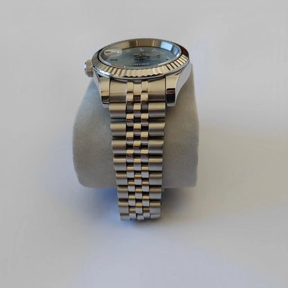 Silver stainless steel Seiko watch with fluted bezel and linked bracelet band on gray cushion.