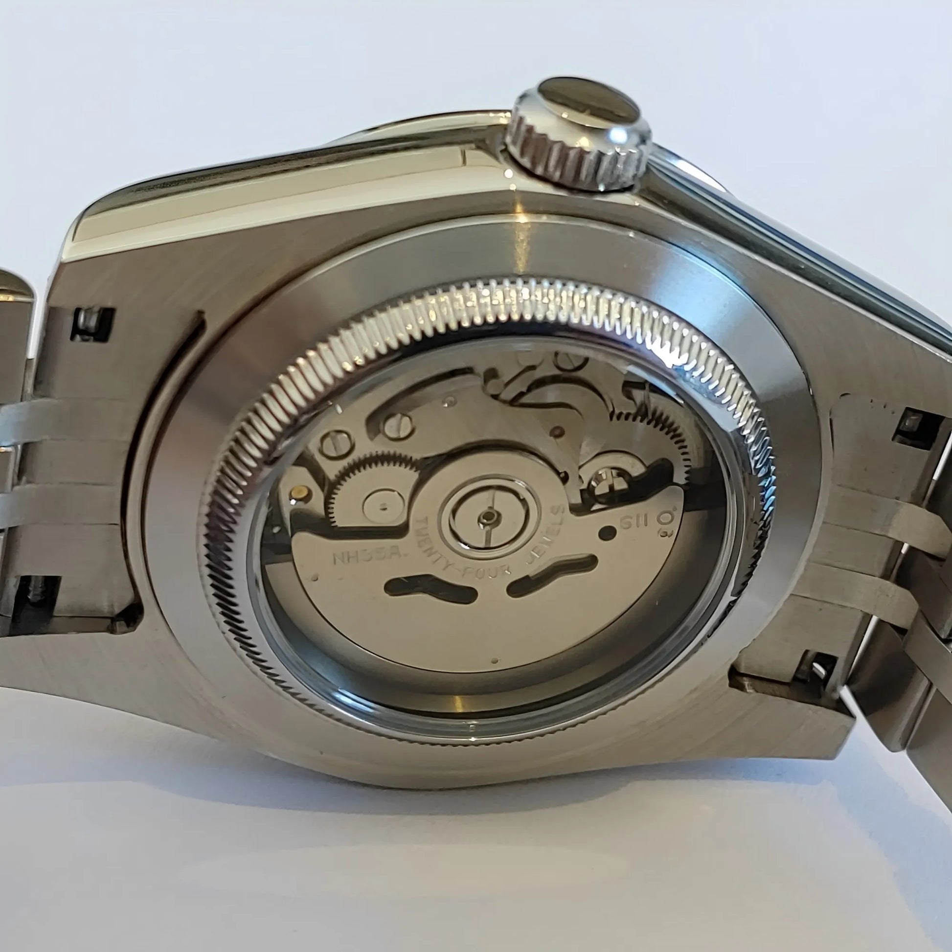 Stainless steel watch case back with exhibition window revealing mechanical movement and fluted edge bezel.