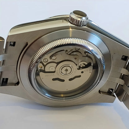 Stainless steel watch case back with exhibition window revealing mechanical movement and fluted edge bezel.