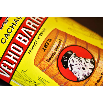 Yellow label with red and white Velho Barreiro text, barrel illustration, and bearded man logo on glass bottle.