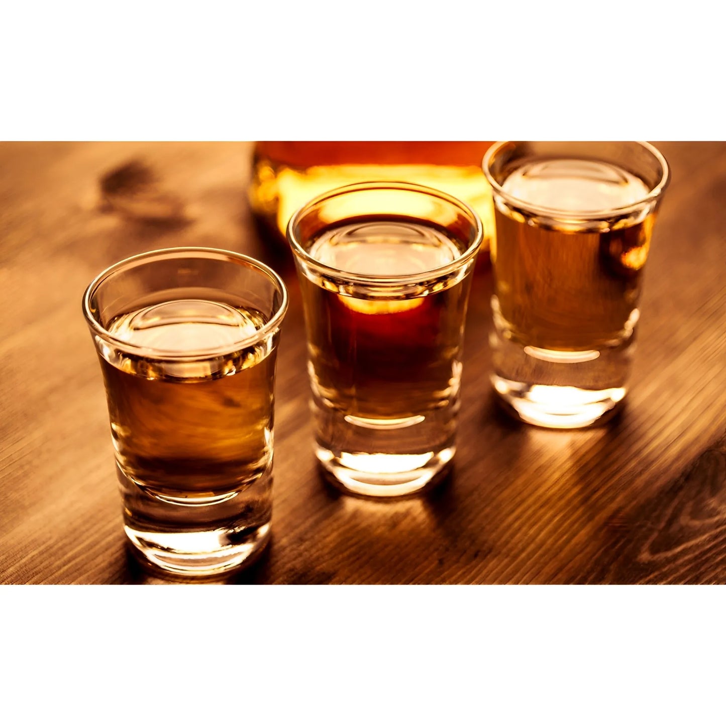 Three clear shot glasses filled with golden amber liquid on a wooden surface with warm lighting.