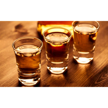 Three clear shot glasses filled with golden amber liquid on a wooden surface with warm lighting.