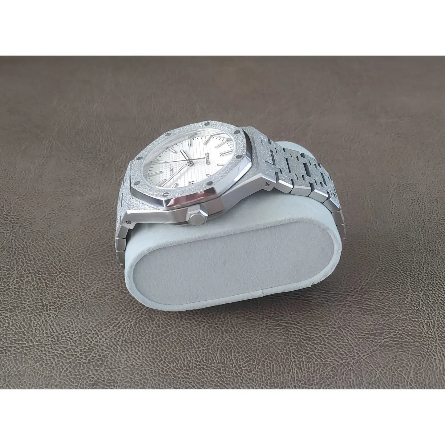 Silver stainless steel watch with frosted white dial, octagonal bezel, and linked bracelet on light gray cushion.