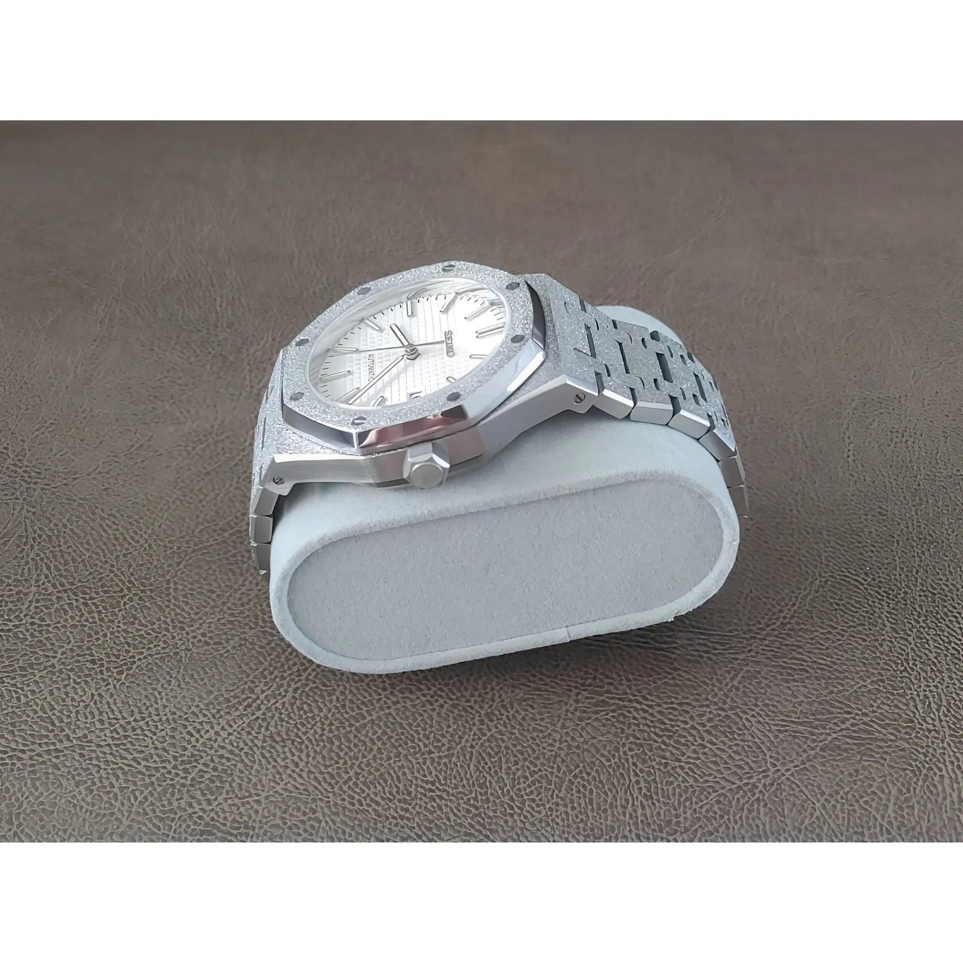 Silver stainless steel watch with frosted white dial, octagonal bezel, and linked bracelet on light gray cushion.