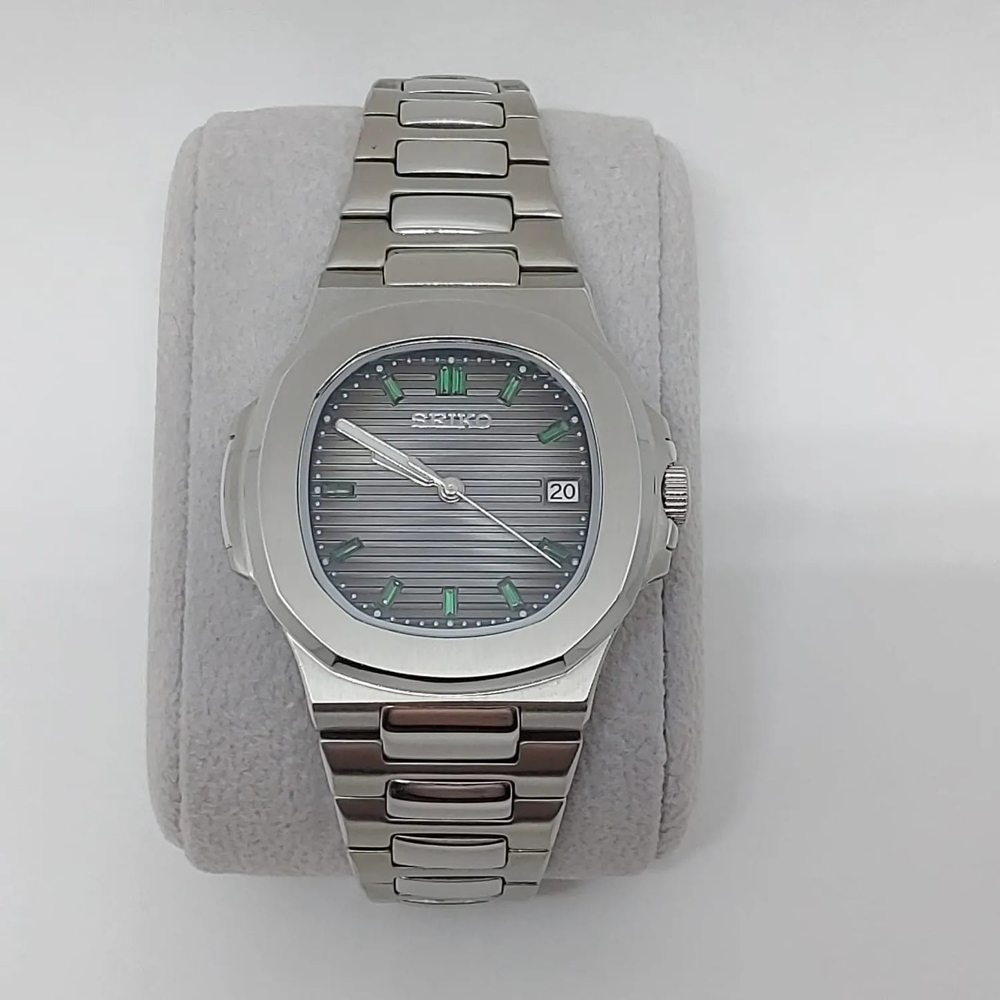 Silver stainless steel Nautilus-style watch with emerald baguette markers and horizontal striped dial.