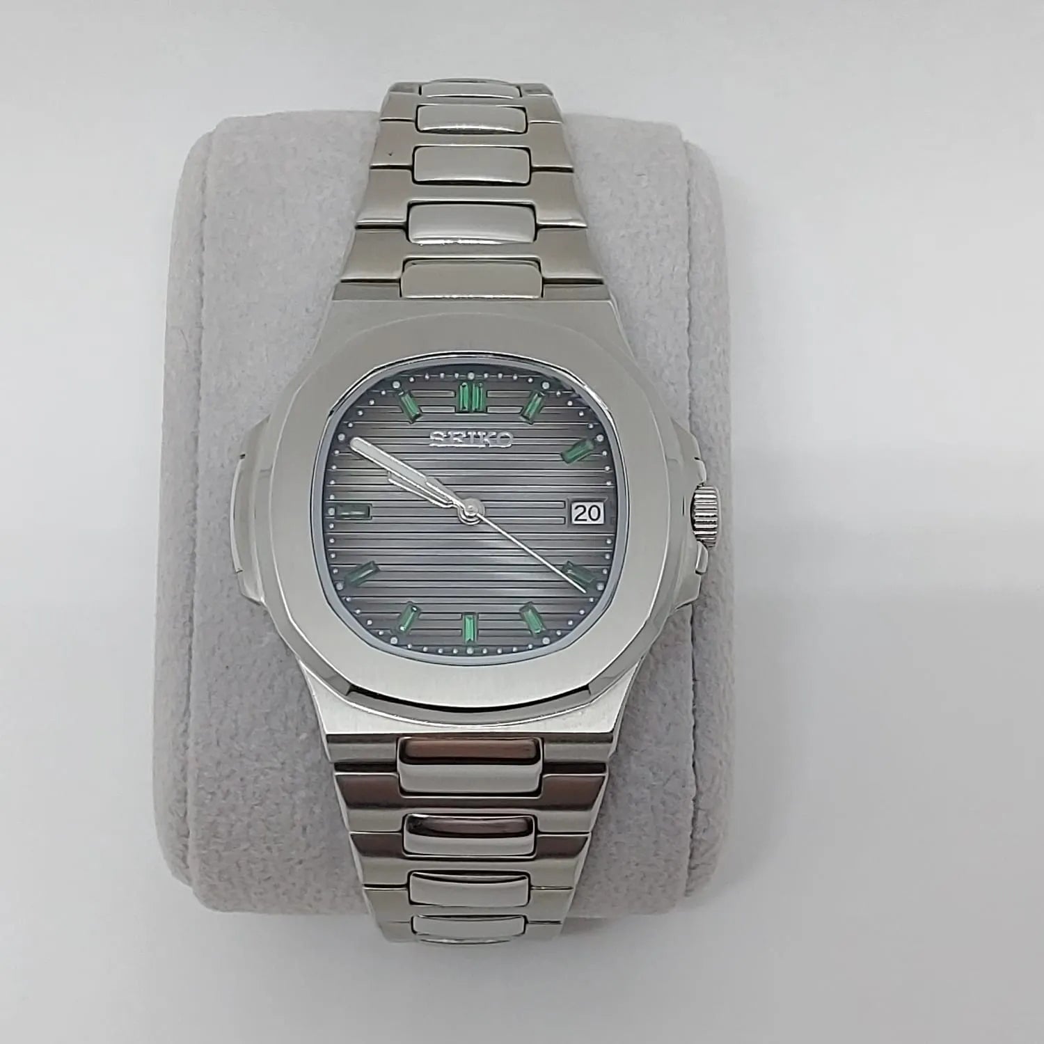 Silver stainless steel Nautilus-style watch with emerald baguette markers and horizontal striped dial.