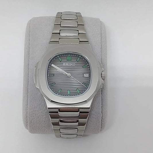 Silver stainless steel Nautilus-style watch with emerald baguette markers and horizontal striped dial.