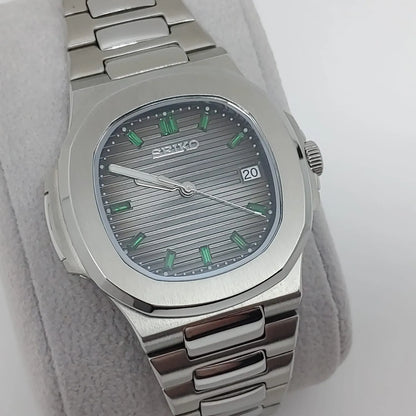 Seiko stainless steel Nautilus-style watch with silver horizontal striped dial and emerald green baguette hour markers.