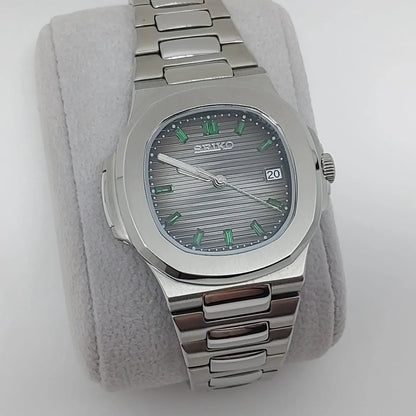 Seiko stainless steel watch with emerald green baguette markers, horizontal textured dial, and date window at 3 o'clock.