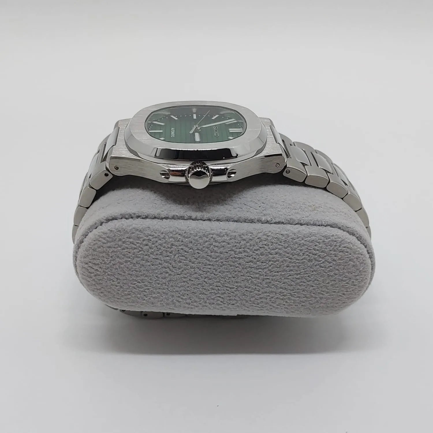 Stainless steel watch with green dial, silver hour markers, and integrated metal bracelet on gray cushion.