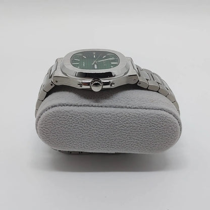 Stainless steel watch with green dial, silver hour markers, and integrated metal bracelet on gray cushion.