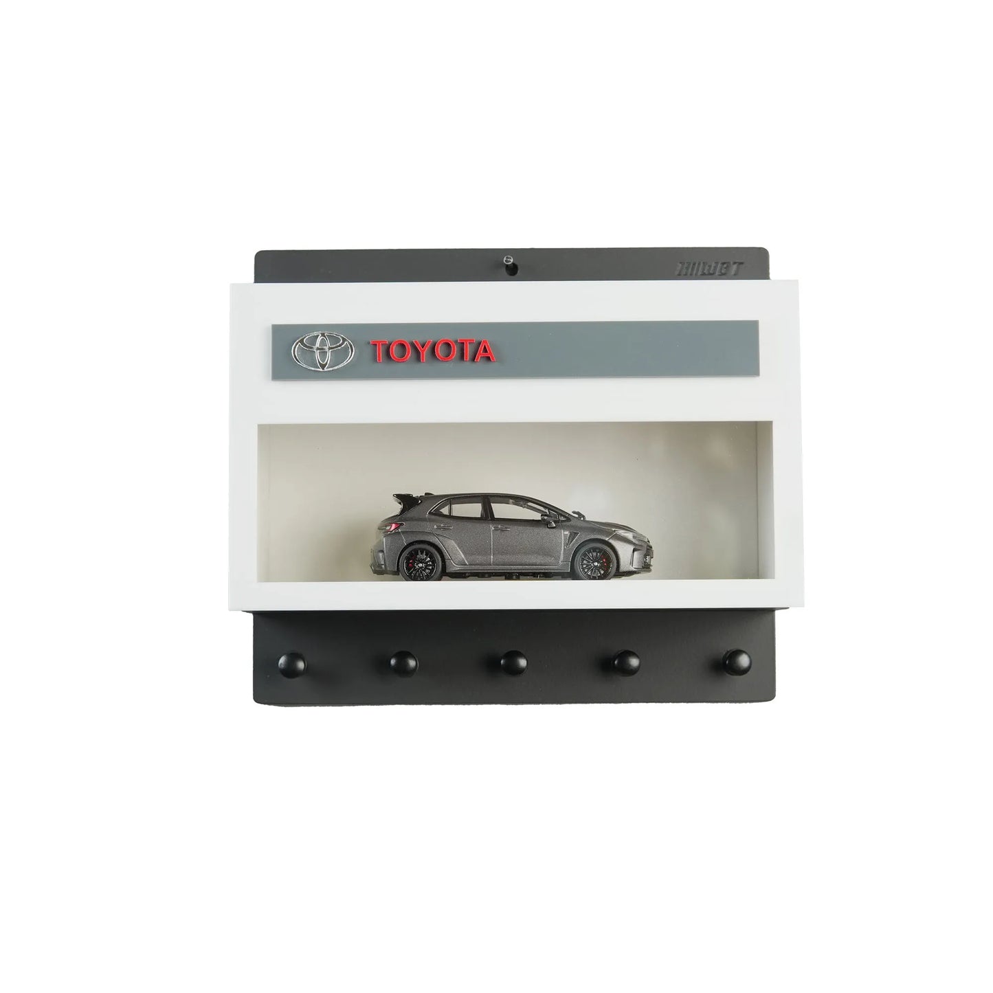 Black and white Toyota wall key hook rack with a gray scale model car inside a display case and five hooks below.