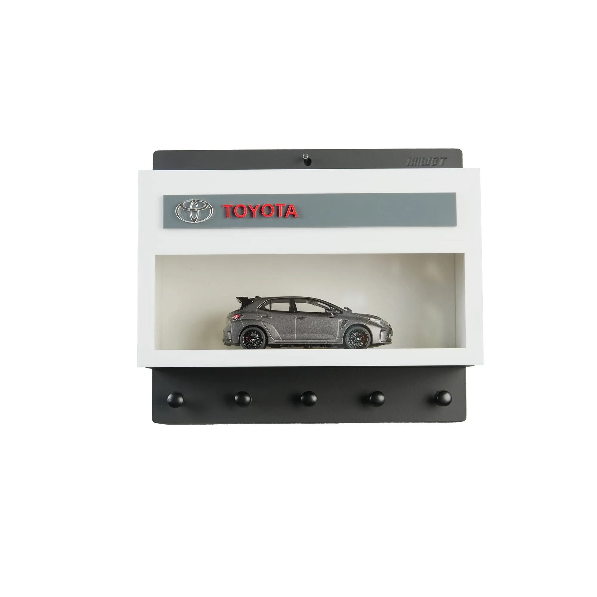 Black and white Toyota wall key hook rack with a gray scale model car inside a display case and five hooks below.