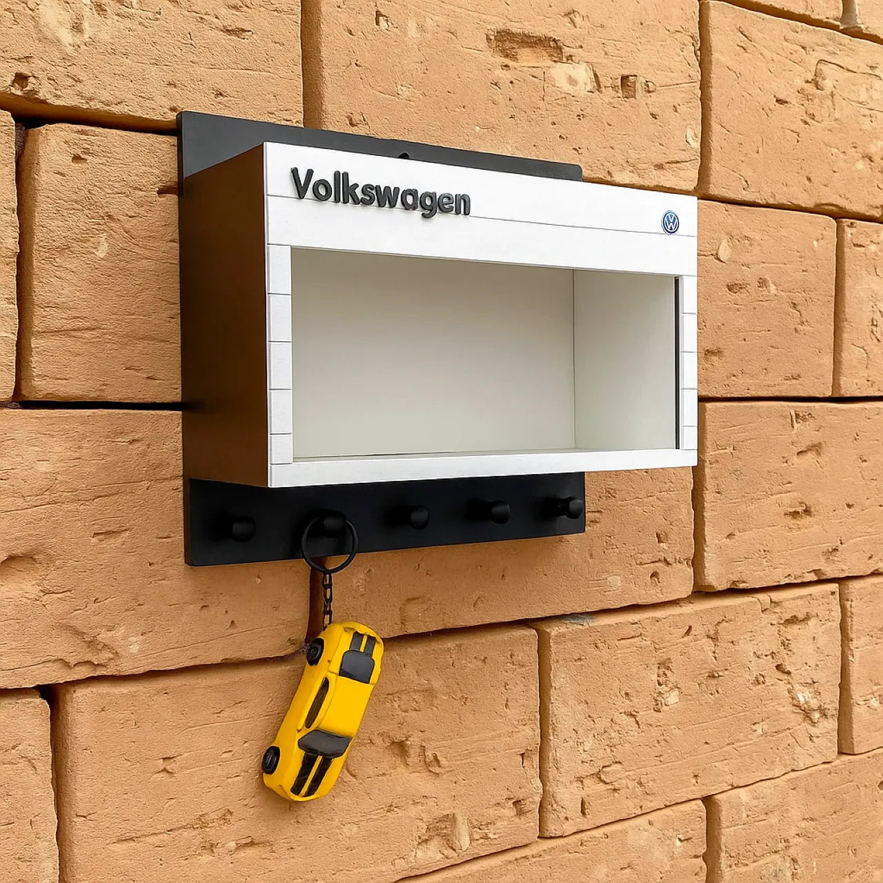 White and black Volkswagen wall-mounted key hook rack with three black hooks and a yellow car keychain hanging on one hook.