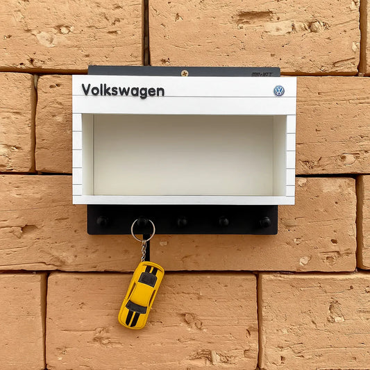 White Volkswagen wall key hook rack with black hooks and a yellow toy car keychain hanging on one hook.