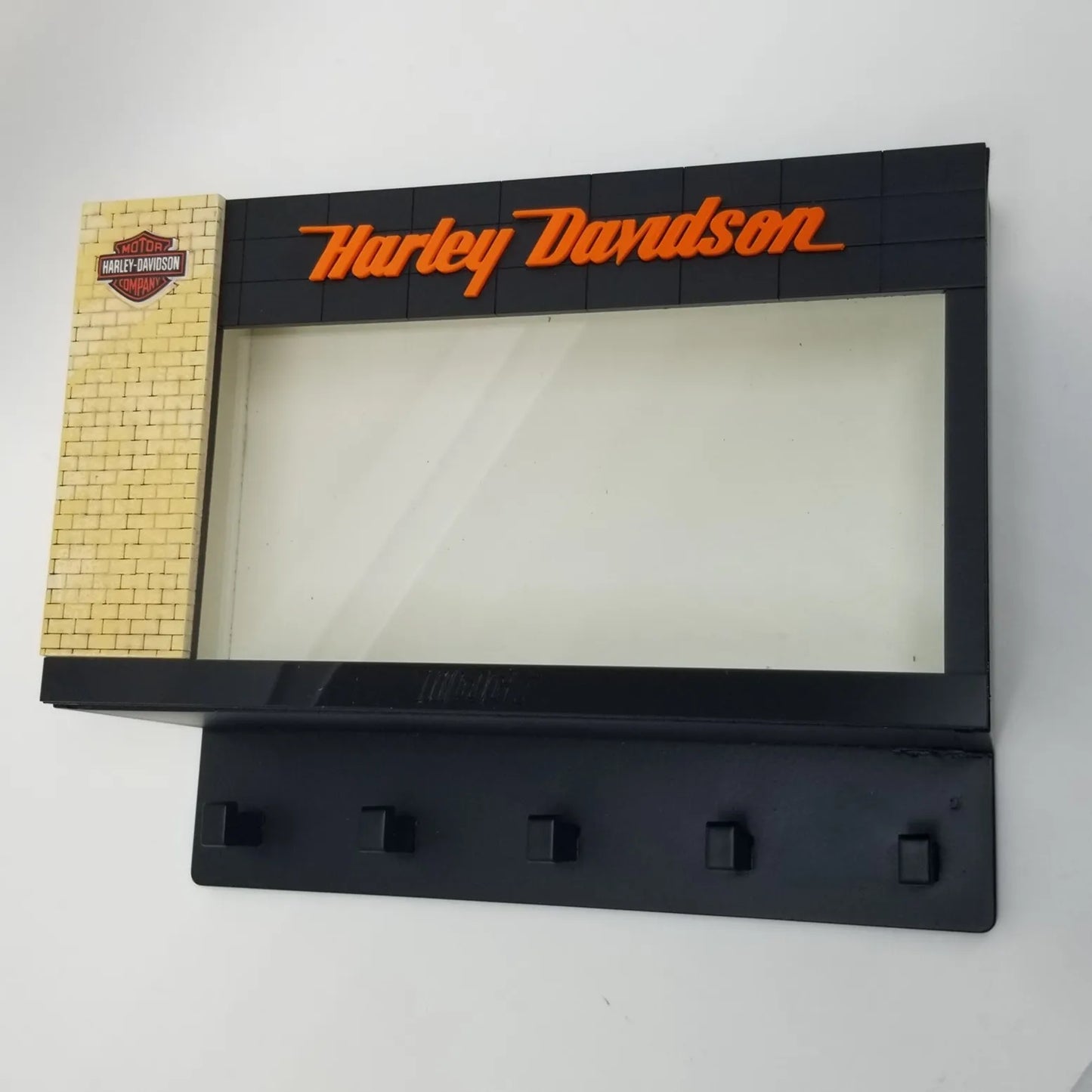 Black Harley Davidson wall key hook rack with orange logo and five hooks below a clear display case.