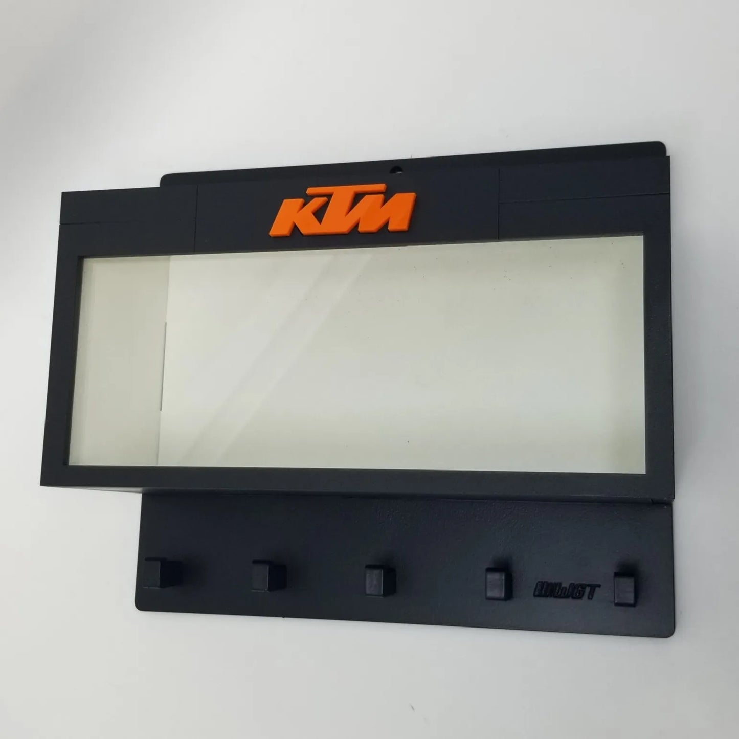 Black KTM wall key hook rack with orange logo and five hooks beneath a clear display case area.