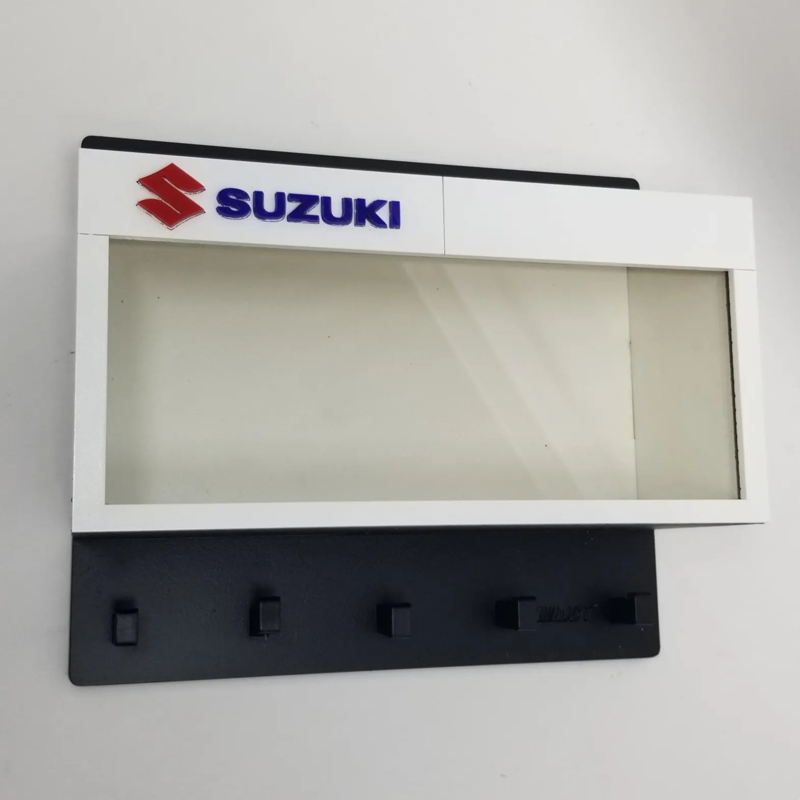 White and black Suzuki wall key hook rack with five hooks and a clear display case above.