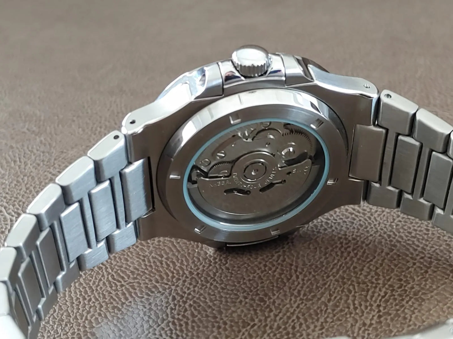 Stainless steel watch with visible automatic movement through transparent back case and linked metal bracelet.