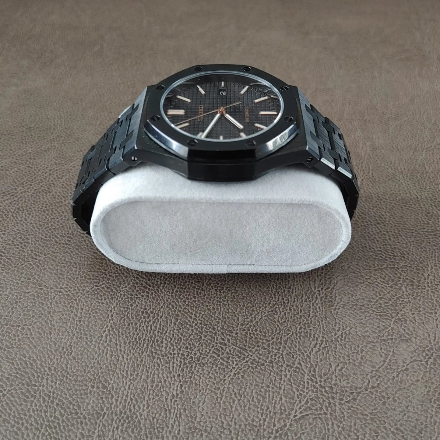 Black and rose gold wristwatch with octagonal bezel and metal link bracelet on white cushion.