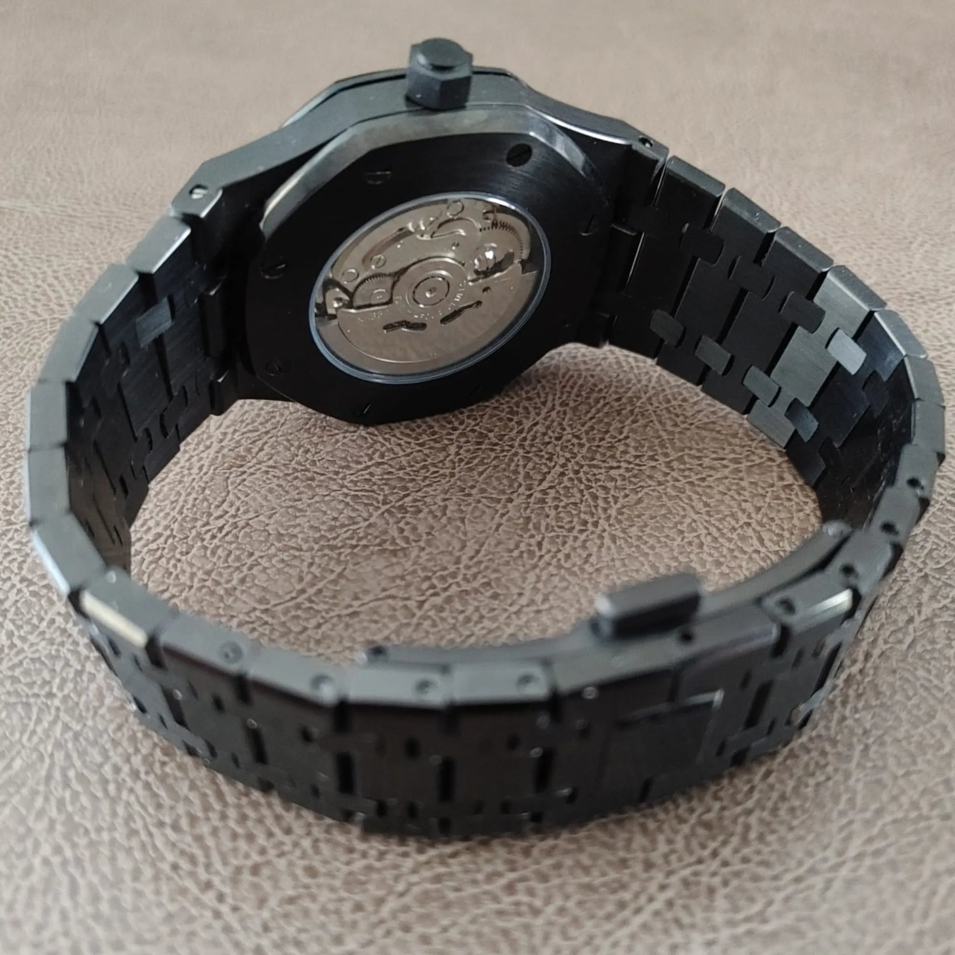 Black metal watch band with rose gold-accented watch back and visible mechanical movement.