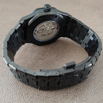 Black metal watch band with rose gold-accented watch back and visible mechanical movement.