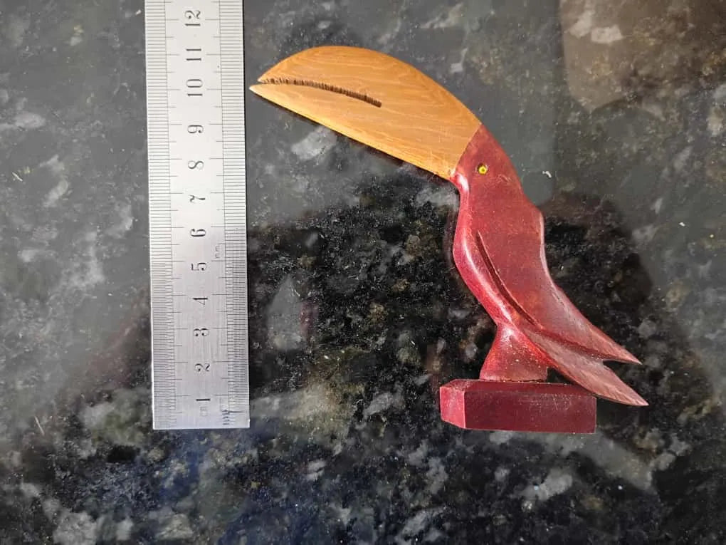 Handcrafted wooden toucan sculpture in red and natural brown Brazilwood with a long curved beak next to a metal ruler.