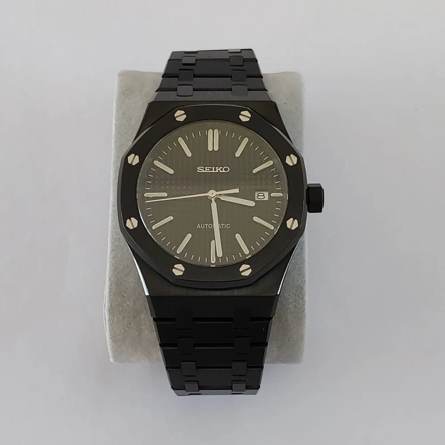 Black stainless steel Seiko watch with octagonal bezel, silver hour markers, and date display at 3 o'clock.