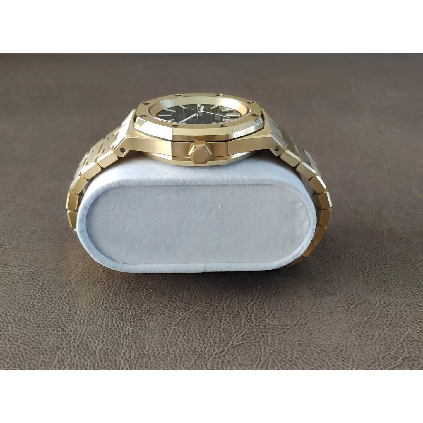 Gold-tone stainless steel watch with black dial, octagonal bezel, and linked bracelet on a gray cushion.