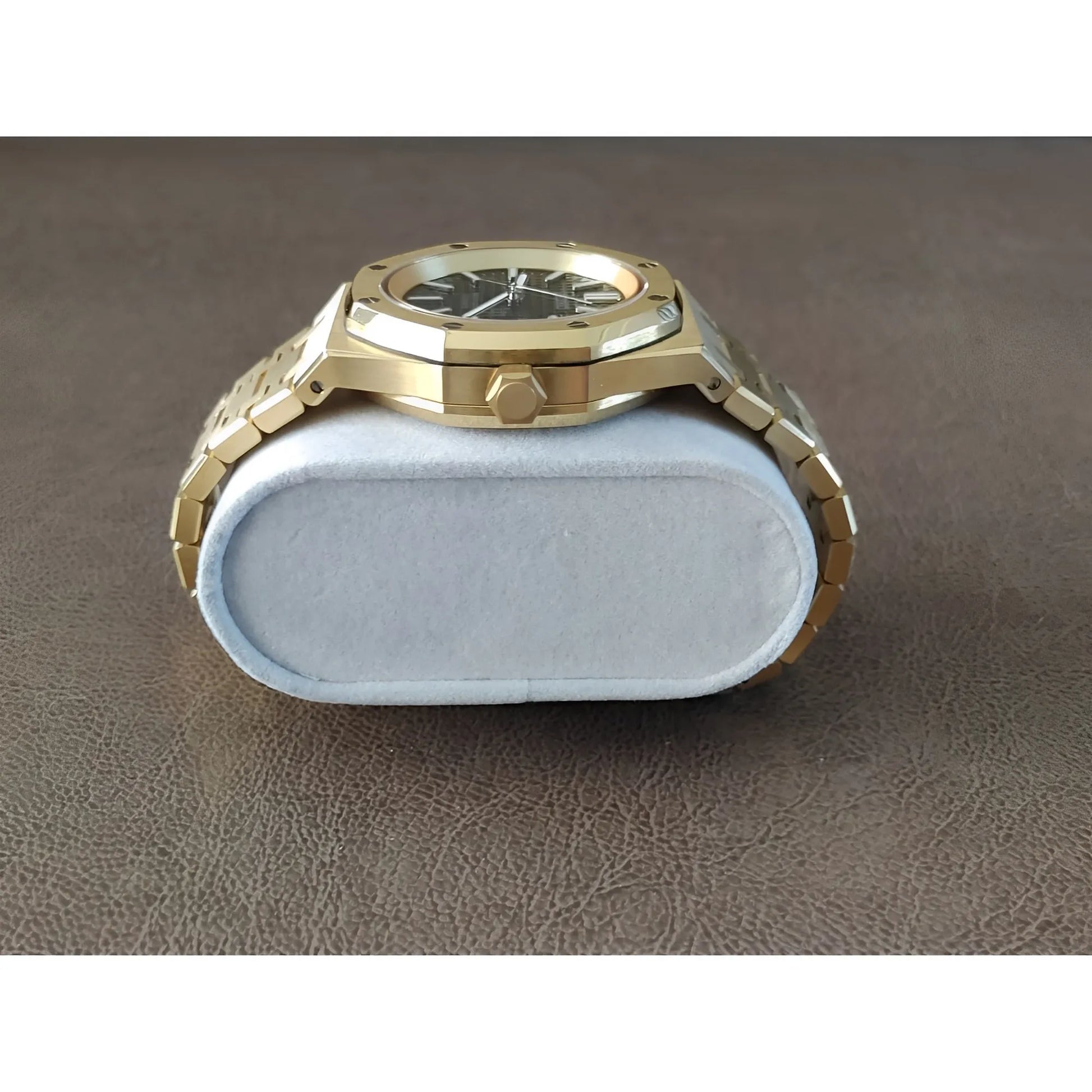 Gold-tone stainless steel watch with black dial, octagonal bezel, and linked bracelet on a gray cushion.