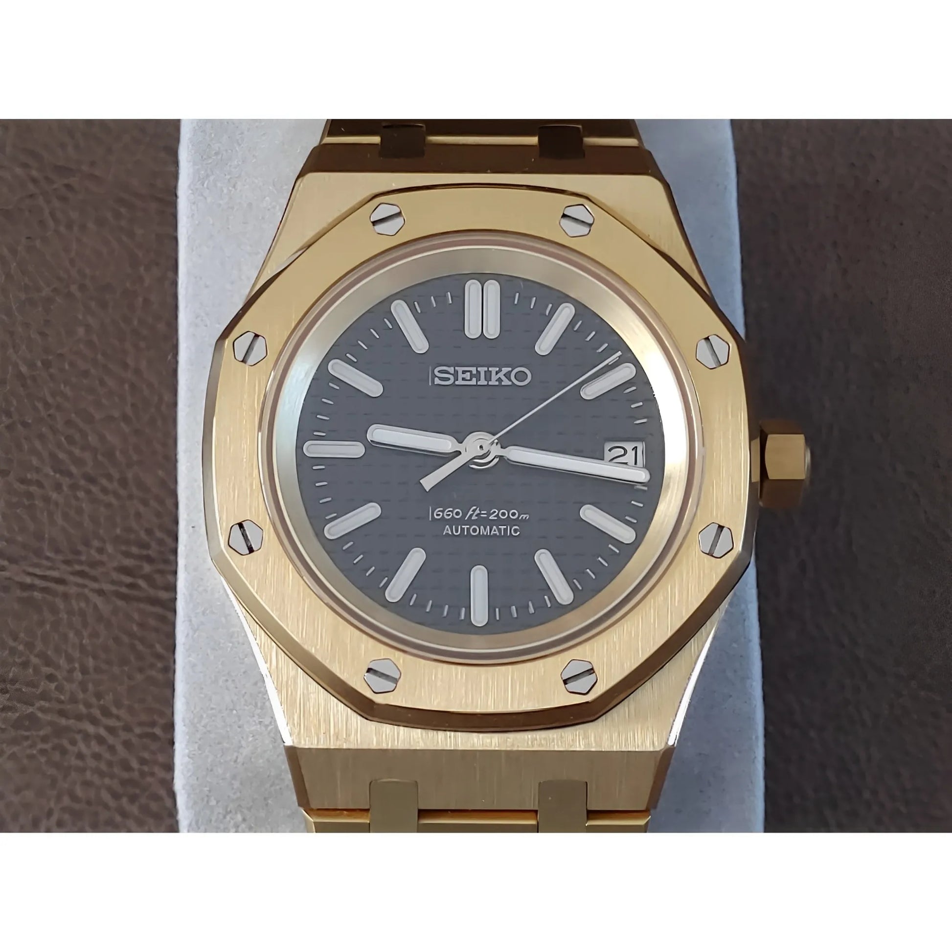 Gold-tone Seiko watch with black dial, luminescent hands, date window, and octagonal bezel with screws.