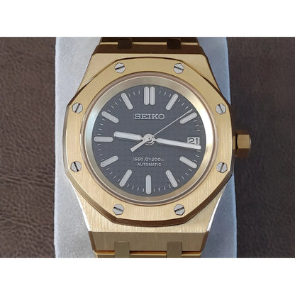 Gold-tone Seiko watch with black dial, luminescent hands, date window, and octagonal bezel with screws.