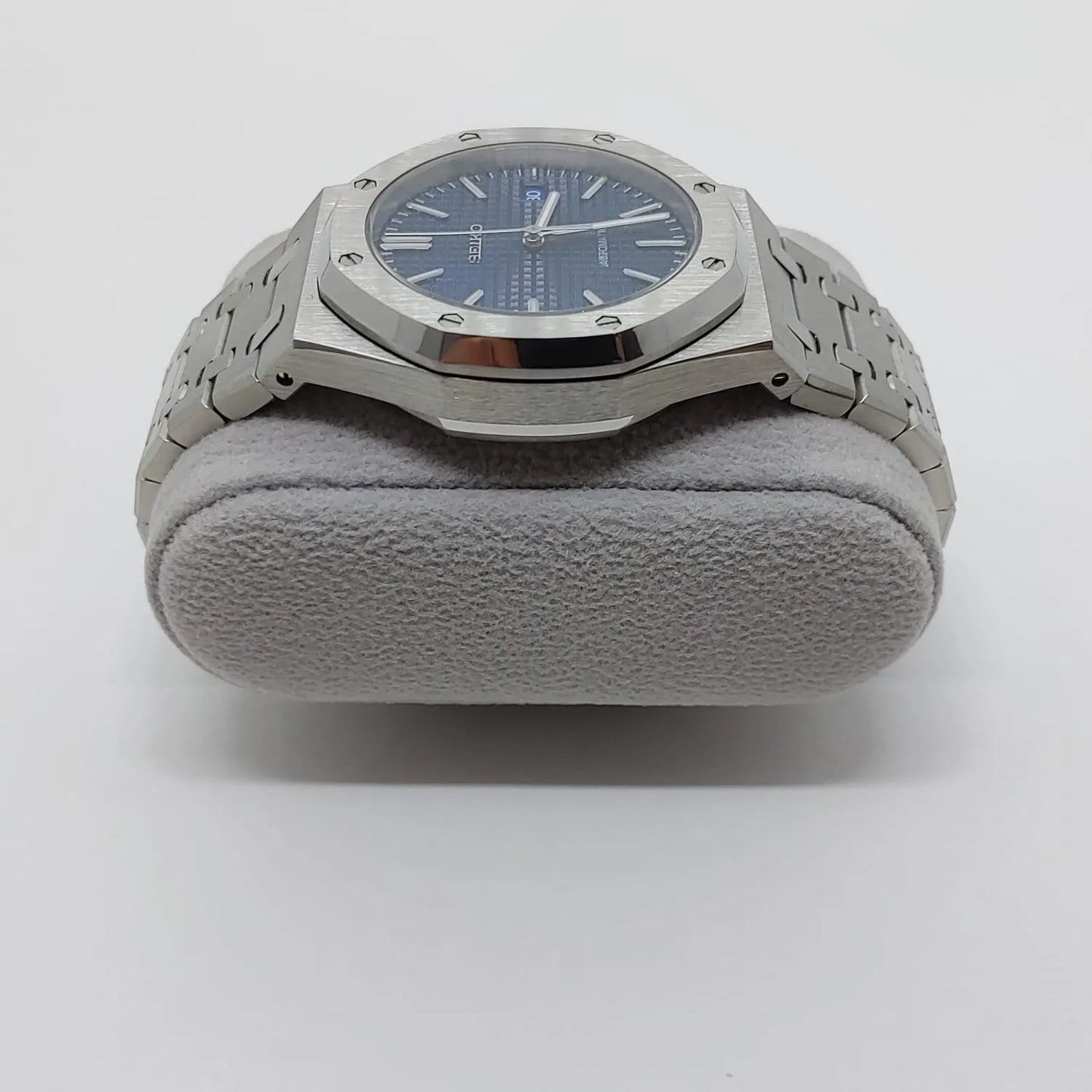 Seiko NH35 watch with navy blue octagonal dial, silver stainless steel case, and linked bracelet on a gray cushion.