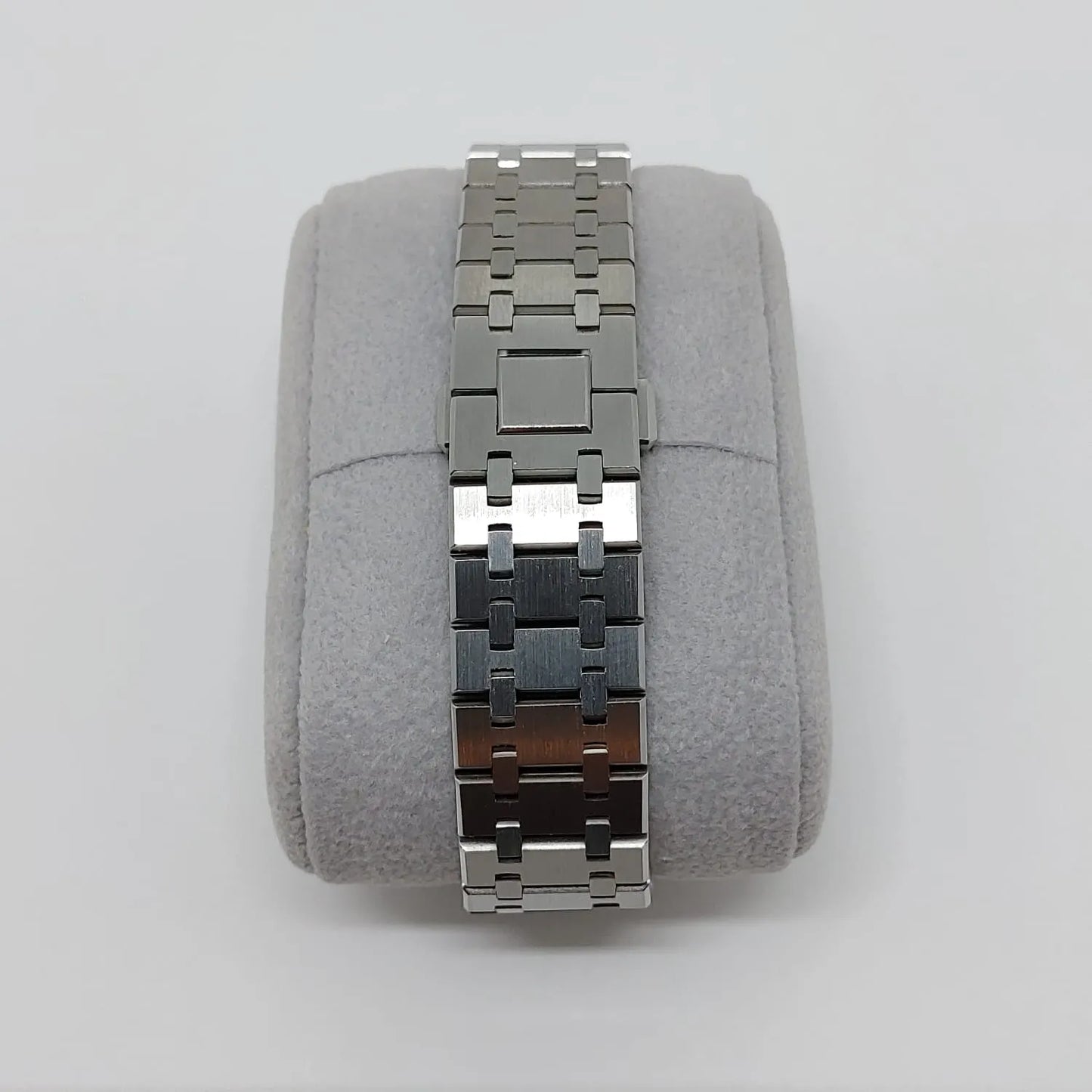 Stainless steel watch bracelet with polished and brushed links on a gray cushion display.