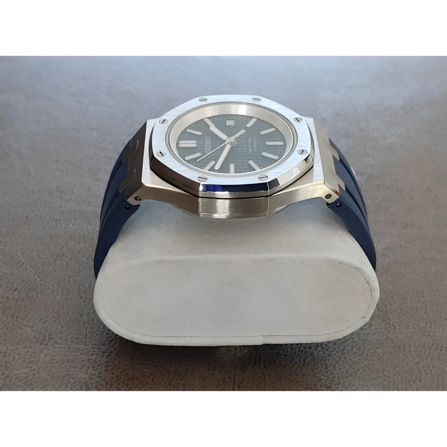 Silver stainless steel bezel watch with navy blue dial and rubber strap on gray surface.